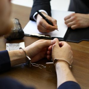 Police officer interrogating criminal in handcuffs at desk indoors