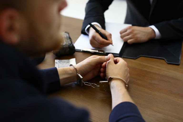 Police officer interrogating criminal in handcuffs at desk indoors