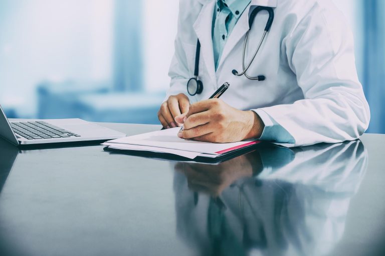 Male doctor sitting at table and writing on a document report in hospital office. Medical healthcare staff and doctor service.