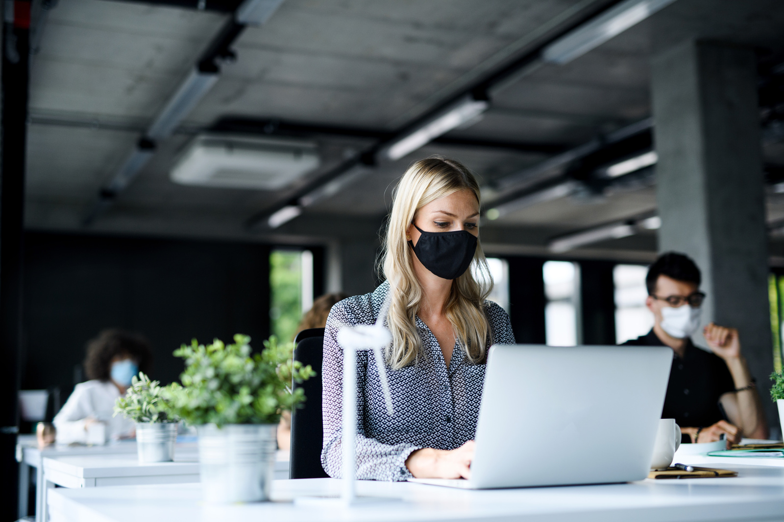 Young people with face masks back at work in office after coronavirus quarantine and lockdown.